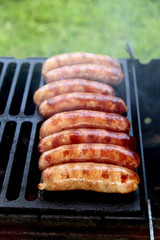 Juicy sausages roasted on the grill barbecue fire on a green grass background