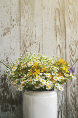 Bouquet of field camomiles. Summer meadow flowers in a white jug against the background of a wooden old board