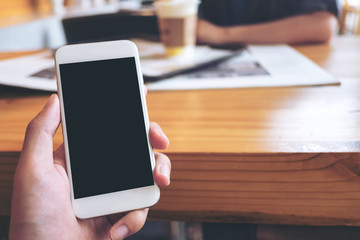 Mockup image of a man's hand holding white mobile phone with blank black screen in modern cafe and blur woman in background
