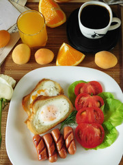 Fried eggs with sausages and tomatoes on a white plate surrounded by apricots and oranges . Breakfast concept