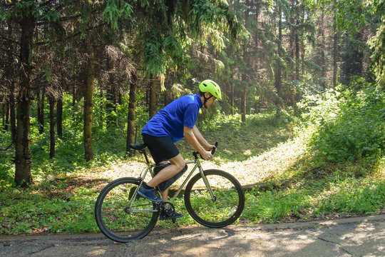 Cyclist with green helmet on a mountain road in forest. Black bicycle