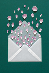 White open envelope with a message in the form of rose petals on a green paper background. The concept of a love story.