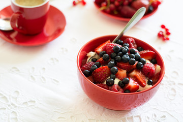 Healthy breakfast: cottage cheese with sour cream, strawberry, raspberry and blueberry, espresso, cherry cheesecake and plate of fresh ripe berries on white table cloth. Selective focus