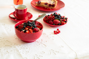 Healthy breakfast: cottage cheese with sour cream, strawberry, raspberry and blueberry, espresso, cherry cheesecake and plate of fresh ripe berries on white table cloth. Selective focus
