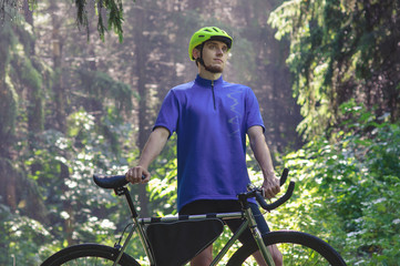 Cyclist with green helmet on a mountain road in forest. Black bicycle