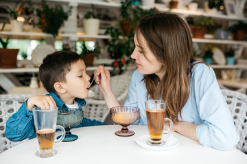 Mom feeds his little son to ice cream in  light cafe