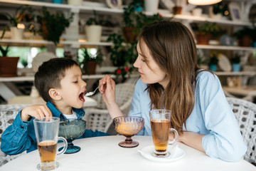 Mom feeds his son to ice cream in a cozy light cafe