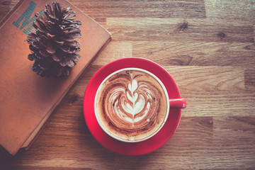Coffee latte art in red cup with textbook on wood table