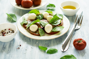 Plate of fresh caprese salad with black tomatoes, mini mozzarella and basil leaves on blue wooden table. Selective focus