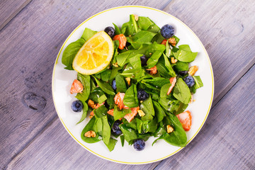 Salmon, spinach, blueberries and walnuts salad on white plate. View from above, top studio shot