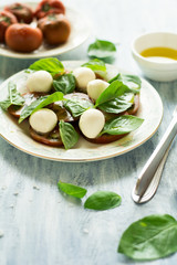 Plate of fresh caprese salad with black tomatoes, mini mozzarella and basil leaves on blue wooden table. Selective focus