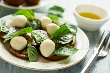 Plate of fresh caprese salad with black tomatoes, mini mozzarella and basil leaves on blue wooden table. Selective focus