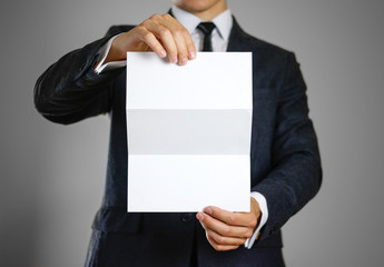 A man in black suit holding blank clear white of the sheet. Closeup. Isolated