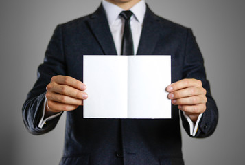 A man in black suit holding blank clear white of the sheet. Closeup. Isolated