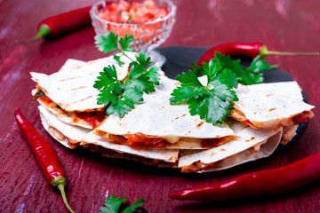 Mexican quesadilla with salsa on black slate stone plate on red wooden background. Chili pepper.