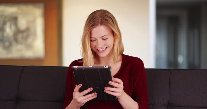 Beautiful Caucasian woman laughing on a couch and looking at a digital pad