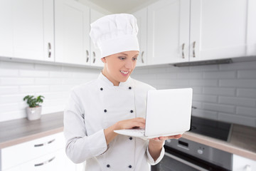 young woman chef in uniform with laptop in modern kitchen