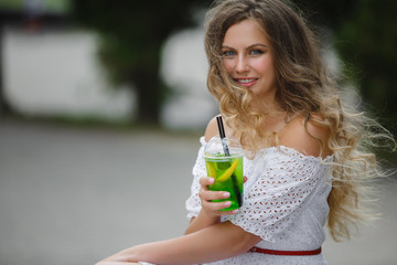 Portrait of a young beautiful attractive woman outdoors in the summer with a glass of ice-cold juice or drink. Pretty girl outside with fresh mojito
