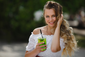 Portrait of a young beautiful attractive woman outdoors in the summer with a glass of ice-cold juice or drink. Pretty girl outside with fresh mojito