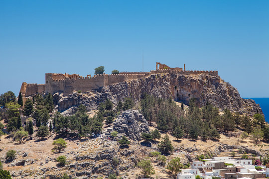 Acropolis on a hill in the city of Lindos. Fragment of residential buildings at the foot of the mountain.