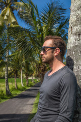 Man standing near empty road with palm trees.