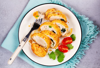 Chicken Kiev garnished with tomato and cilantro. Breaded chicken breast stuffed with herbs and butter on white plate. View from above, top studio shot.
