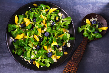 Lamb's lettuce, mango, blueberries and cheese salad on black plate. View from above, top studio shot