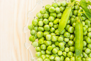 Green peas in a glass plate on a light wooden background