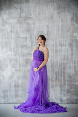 Fototapeta na wymiar beautiful pregnant woman posing in purple dress in Studio