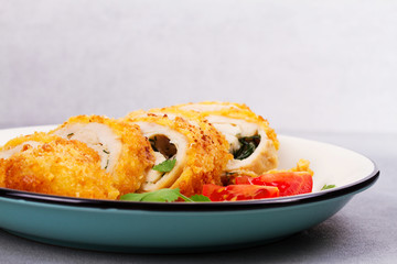 Chicken Kiev garnished with tomato and cilantro. Breaded chicken breast stuffed with herbs and butter on white plate