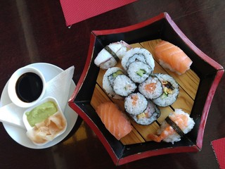 Family dinner in traditional Japanese restaurant. Salmon sushi is served on red wooden plate with wasabi and soy sauce.