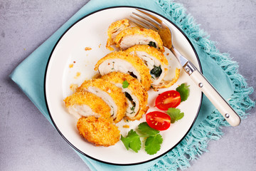 Chicken Kiev garnished with tomato and cilantro. Breaded chicken breast stuffed with herbs and butter on white plate. View from above, top studio shot.