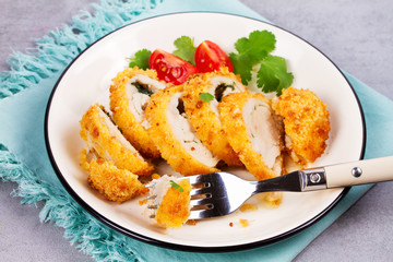 Chicken Kiev garnished with tomato and cilantro. Breaded chicken breast stuffed with herbs and butter on white plate