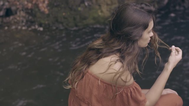Dreamy Bohemian Model Sits Near Water, Plays With Hair, Looks Around 
