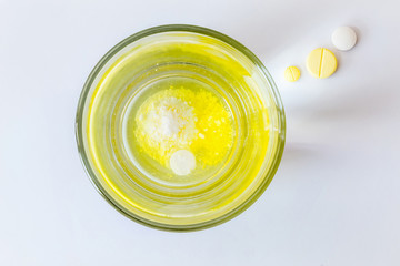 Medicine tablets slow dissolving in glass water and three tablets outside in light beam on white background.