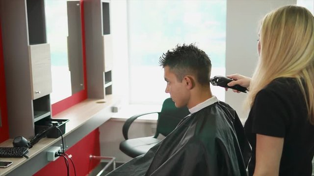 A young and professional hair stylist who works in a hair salon shaves the back of the head of the client who came to change the image.