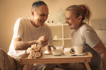 Older couple having breakfast on bed.