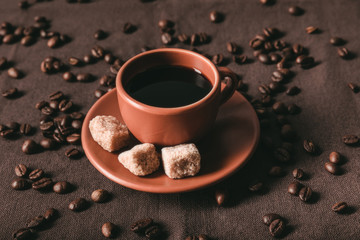 ceramic coffee cup with brown sugar cubes and scattered coffee grains on brown cloth