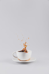 coffee splashing out of white cup on saucer, isolated on grey with copy space