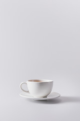 white cup with aromatic coffee on saucer isolated on grey with copy space