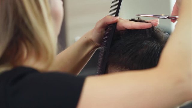 close up shot of the stylist hands, who cuts the dark hair of a young man, a visitor to a beauty salon changes her hair and immige in barbershop
