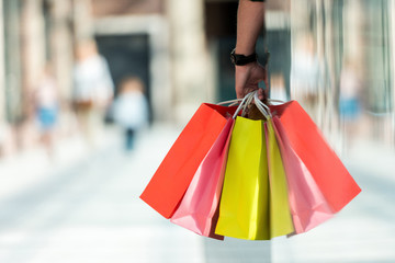 Cropped shot of man holding multicolored paper bags while standing in shopping mall