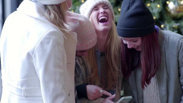 Girls Gather Around Smartphone And Laugh A Lot, In Front Of Christmas Tree (Slow Motion)