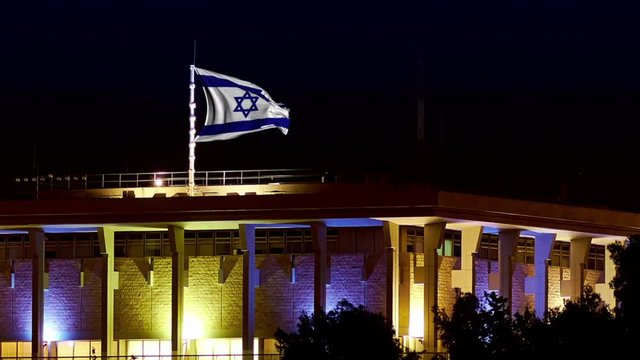 Knesset building the Parliament of Israel with flying waving flag of Israel at night. The Knesset located in Jerusalem and elects both President and Prime Minister and supervises Israeli government