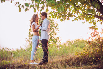 Young kissing couple under big tree at sunset