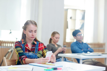 Teenage girl with smartphone texting in classroom by desk