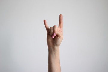 Young woman's hands isolated on light gray background shows sign of the horns. Gesture