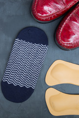 Leather orthopedic insoles, socks and red shoes on stone background. Top view.