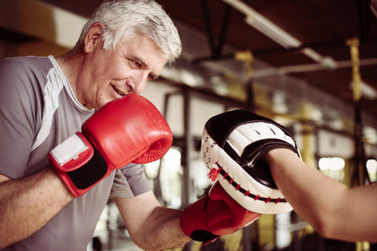 Older Man Boxing In Gym. Senior Man With Personal Trainer.