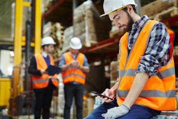 Man in uniform and helmet messaging at break in warehouse